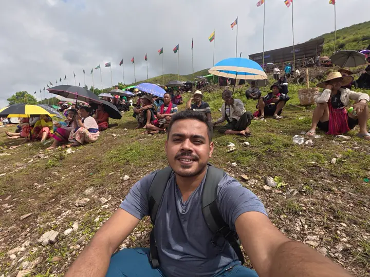 Saif sitting on a hillside among Pa-O villagers under umbrellas, waiting for the rockets at the Pa-O Rocket Festival in Shan State